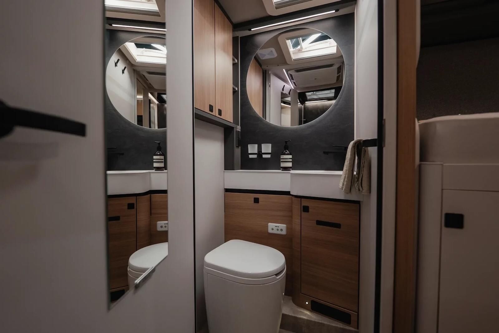 HYMER B-ML I780 - Salle d'eau au design élégant, avec sa paroi imitation ardoise habillée d'un grand miroir circulaire rétroéclairé.